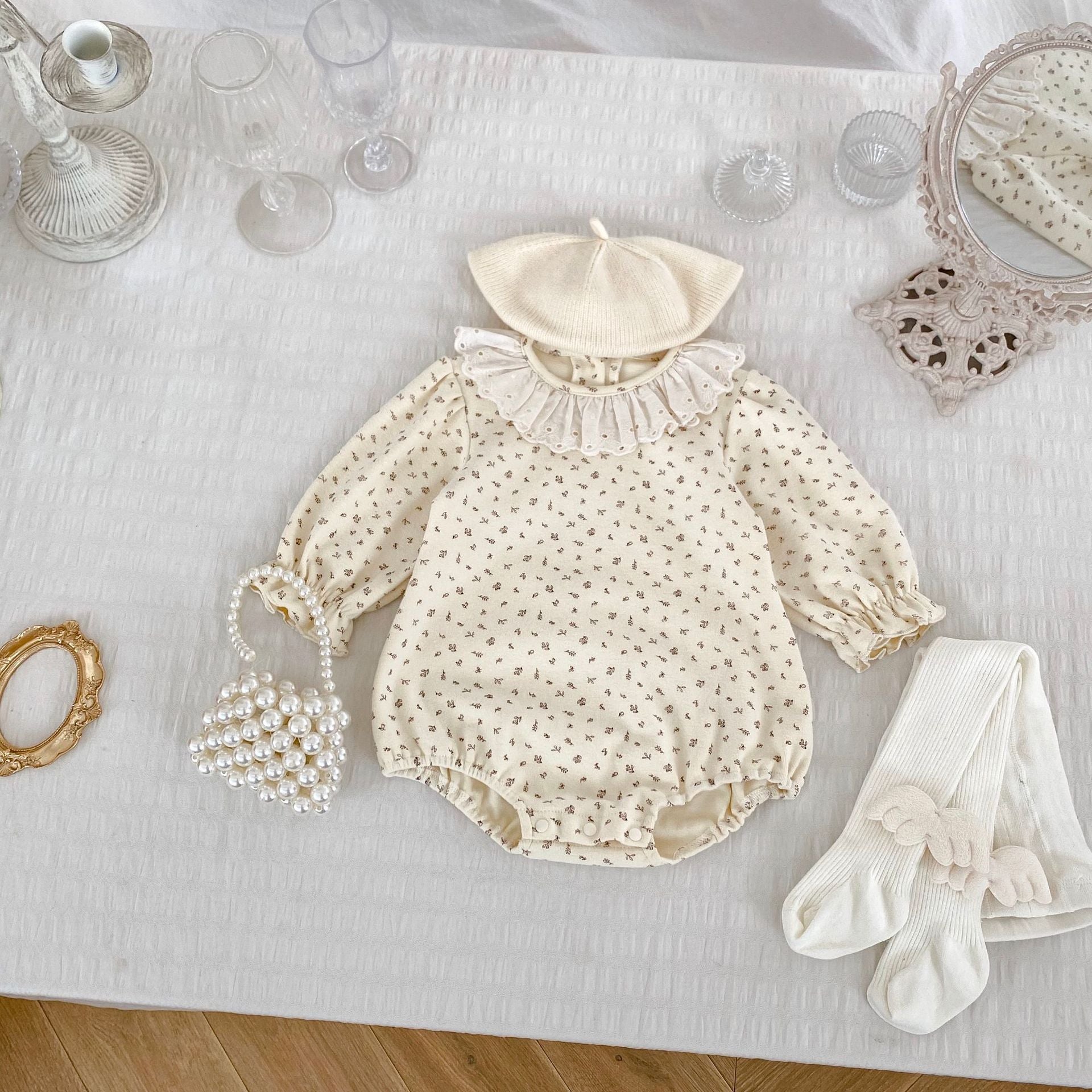 A baby girl wearing a floral print ruffle collar onesie in grey, showcasing long sleeves and a charming design.