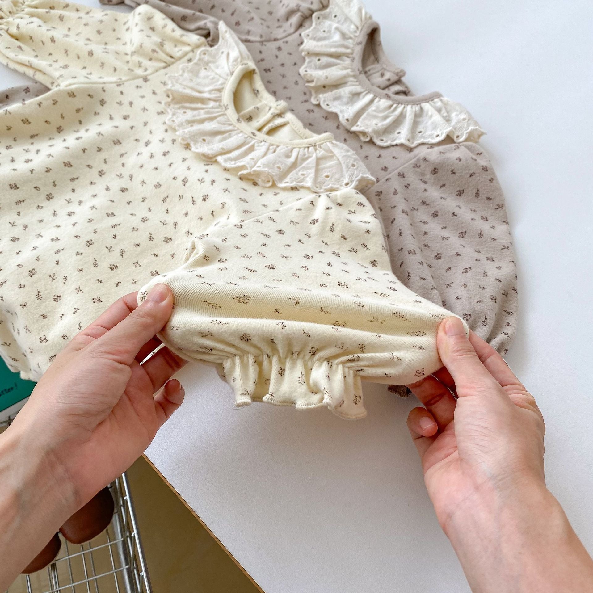 A baby girl wearing a floral print ruffle collar onesie in grey, showcasing long sleeves and a charming design.