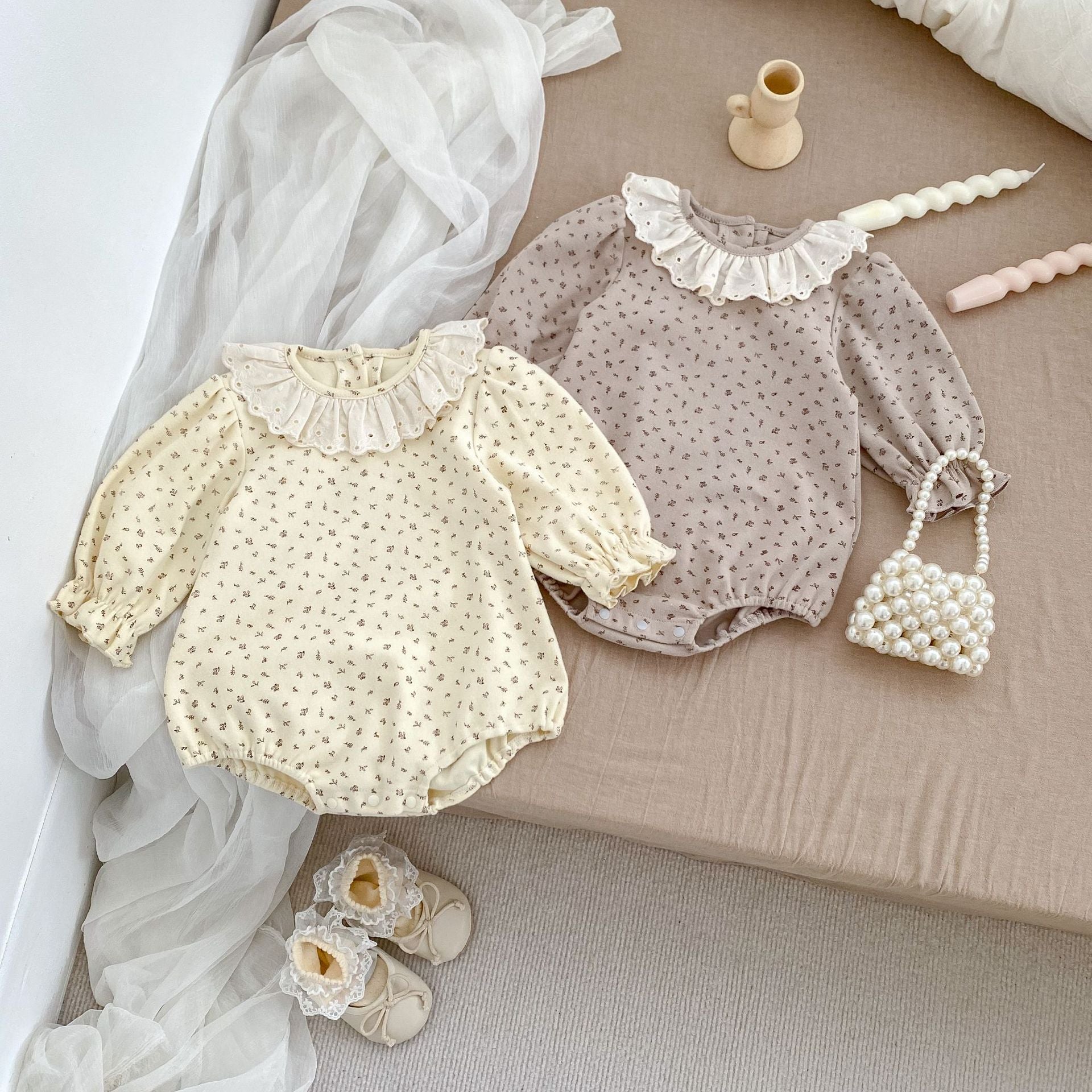 A baby girl wearing a floral print ruffle collar onesie in grey, showcasing long sleeves and a charming design.