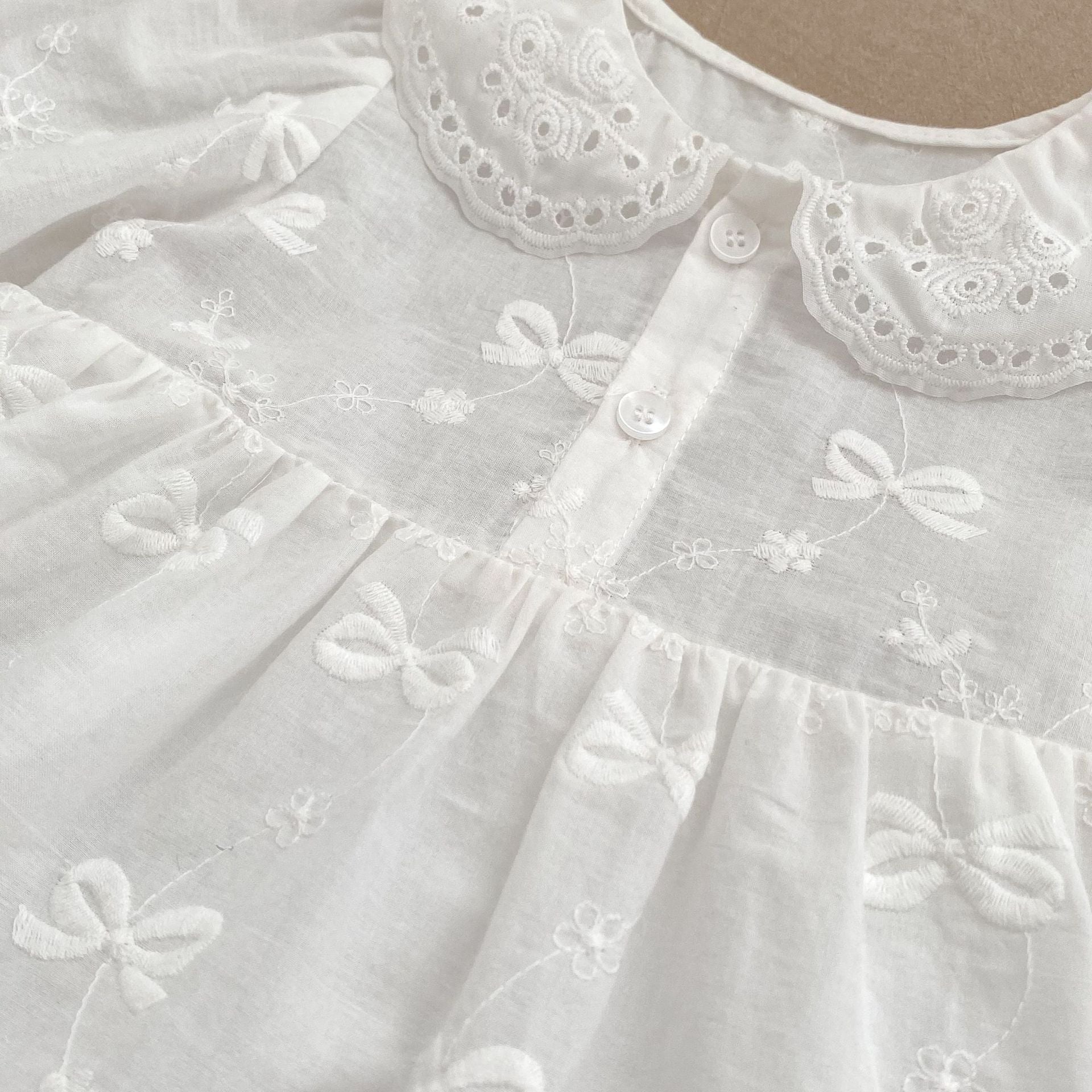 A beige long-sleeve dress for baby girls featuring embroidered bows and flowers, made from soft cotton, suitable for spring and autumn.