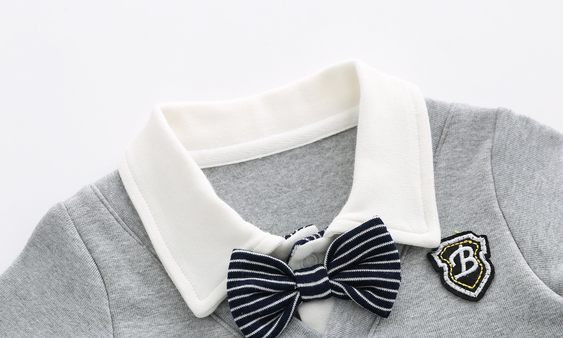 Baby boy wearing a stylish grey striped romper with badge patch and bow tie, showcasing a snap button front design.