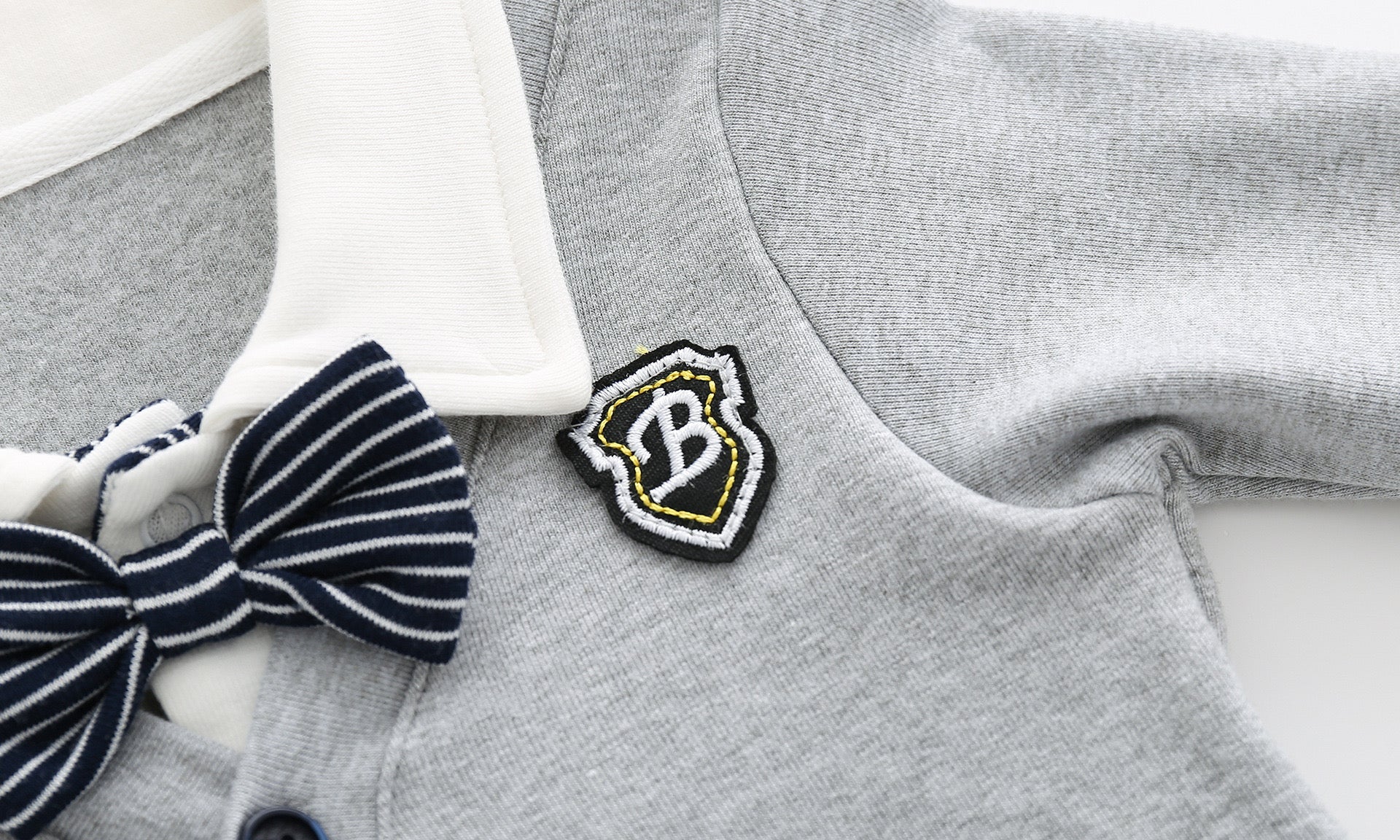 Baby boy wearing a stylish grey striped romper with badge patch and bow tie, showcasing a snap button front design.