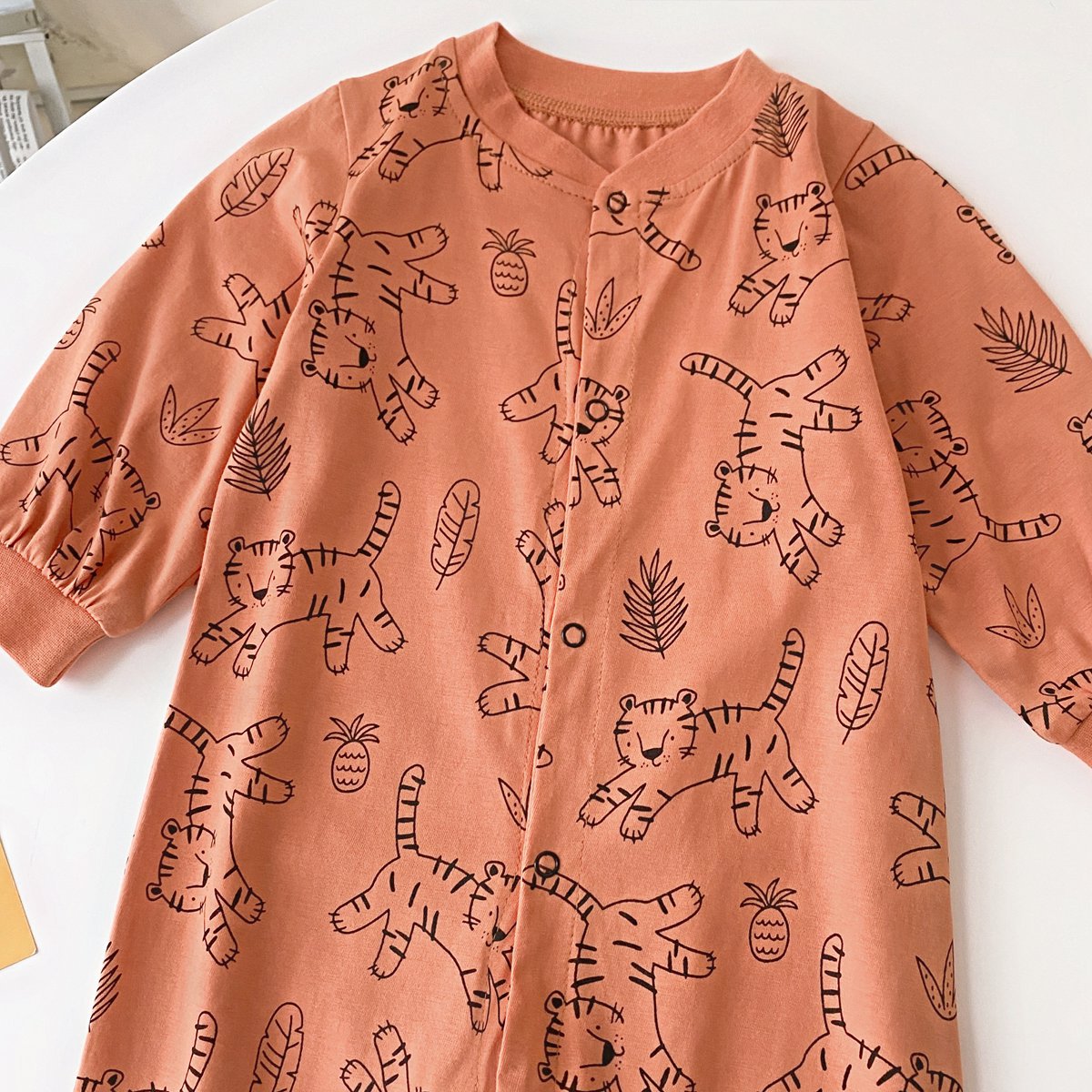 Baby boy wearing a long-sleeved jumpsuit with cartoon animal graphics and snap button front design, showcasing vibrant colors.