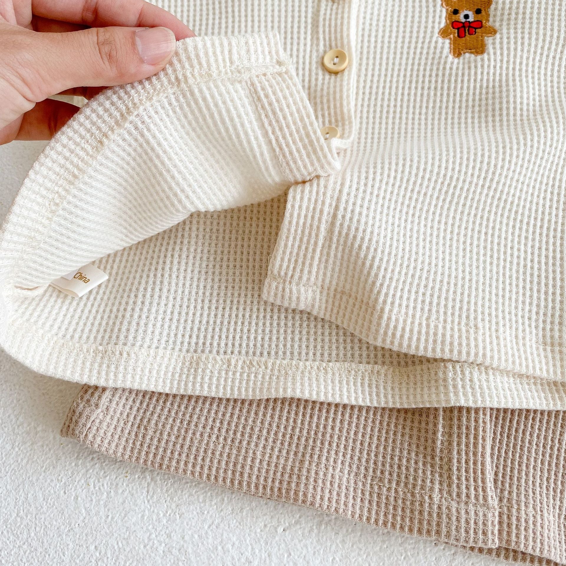 Baby outfit featuring a cartoon bear embroidery, waffle knitted cardigan, and combo pants in khaki and apricot colors.