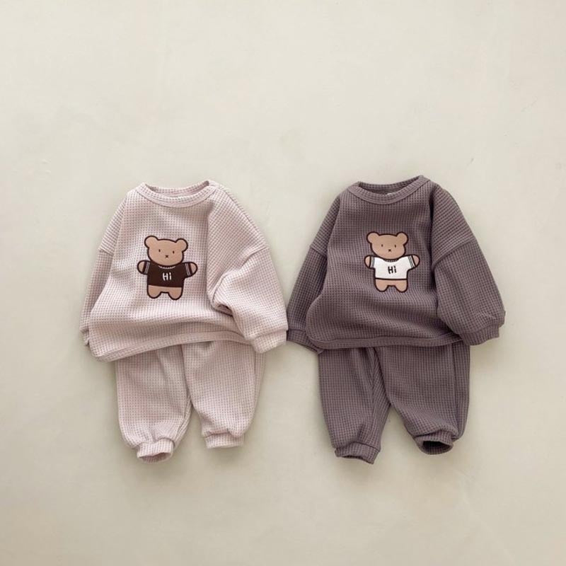 A cute baby wearing a pink hoodie set with an embroidered cartoon bear design, showcasing the waffle fabric texture.