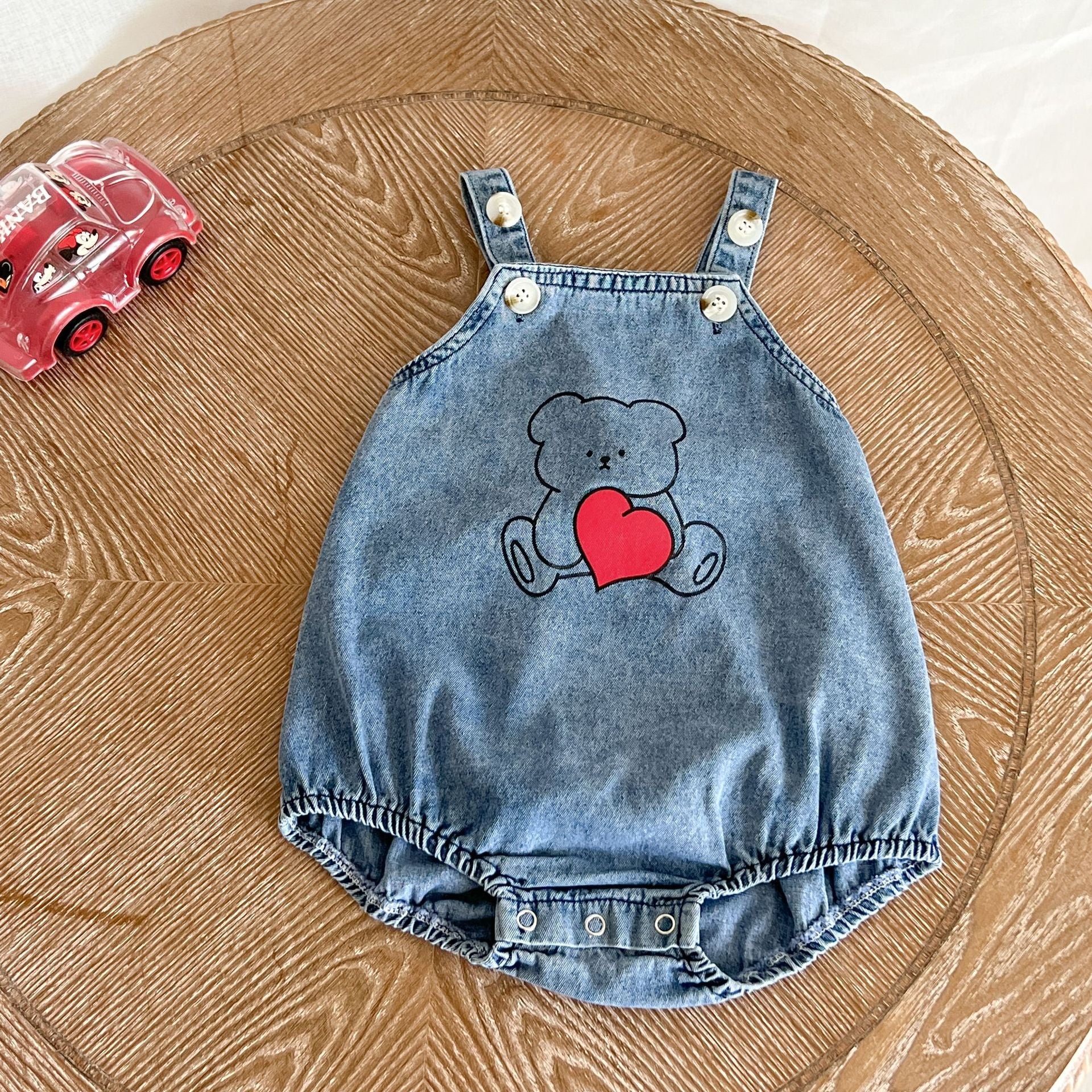 Baby wearing a denim strap onesie with a cartoon bear pattern, showcasing a cute and stylish design.