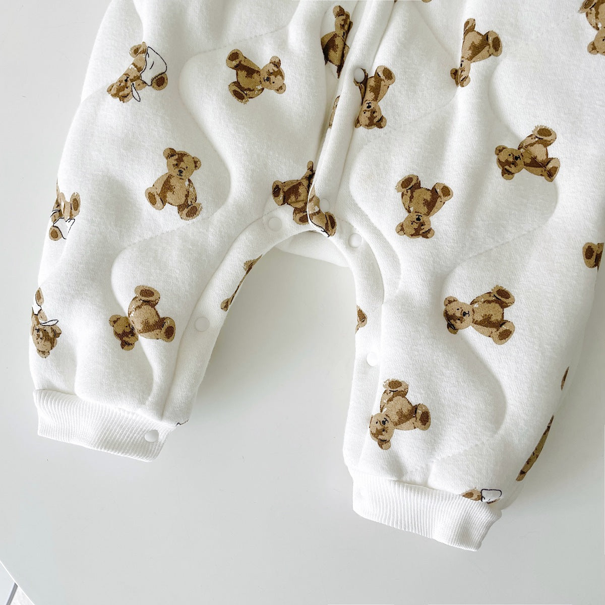 Baby wearing a thickened quilted winter romper with a cartoon bear print, showcasing a cozy and stylish design in white and apricot colors.