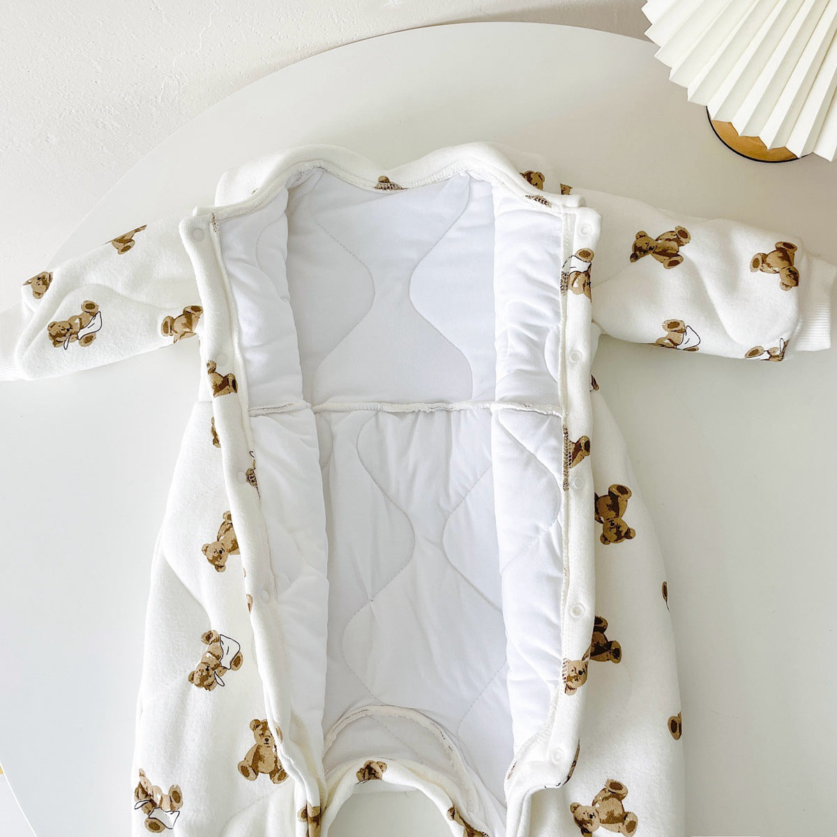 Baby wearing a thickened quilted winter romper with a cartoon bear print, showcasing a cozy and stylish design in white and apricot colors.
