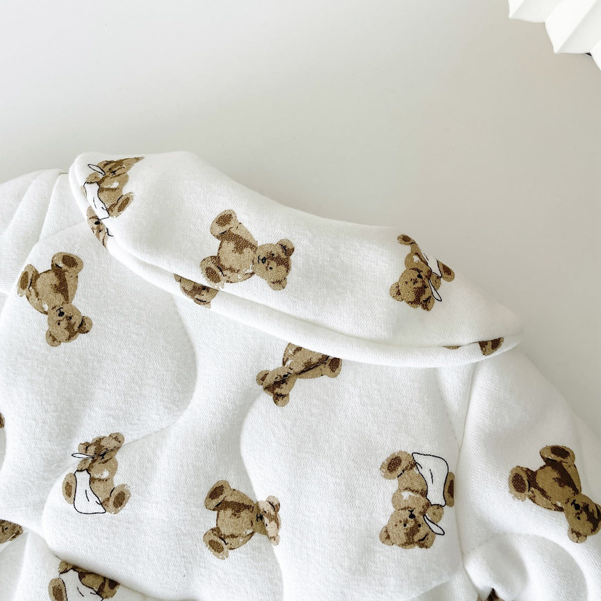 Baby wearing a thickened quilted winter romper with a cartoon bear print, showcasing a cozy and stylish design in white and apricot colors.