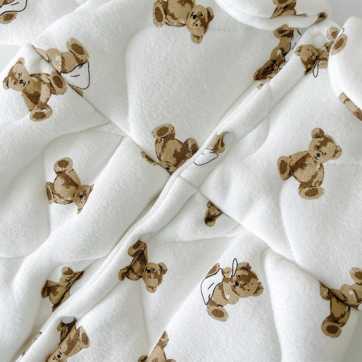 Baby wearing a thickened quilted winter romper with a cartoon bear print, showcasing a cozy and stylish design in white and apricot colors.