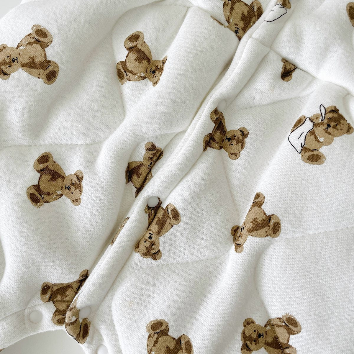 Baby wearing a thickened quilted winter romper with a cartoon bear print, showcasing a cozy and stylish design in white and apricot colors.