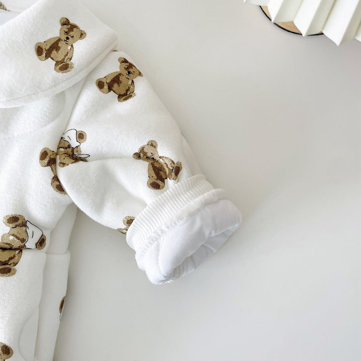 Baby wearing a thickened quilted winter romper with a cartoon bear print, showcasing a cozy and stylish design in white and apricot colors.