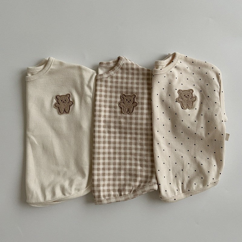 A cute baby shirt featuring a dot pattern and cartoon bear patches, made from soft cotton fabric, available in beige, apricot, and brown colors.