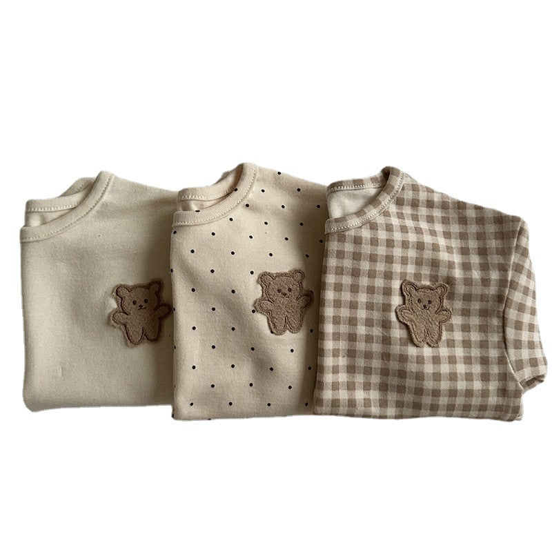 A cute baby shirt featuring a dot pattern and cartoon bear patches, made from soft cotton fabric, available in beige, apricot, and brown colors.