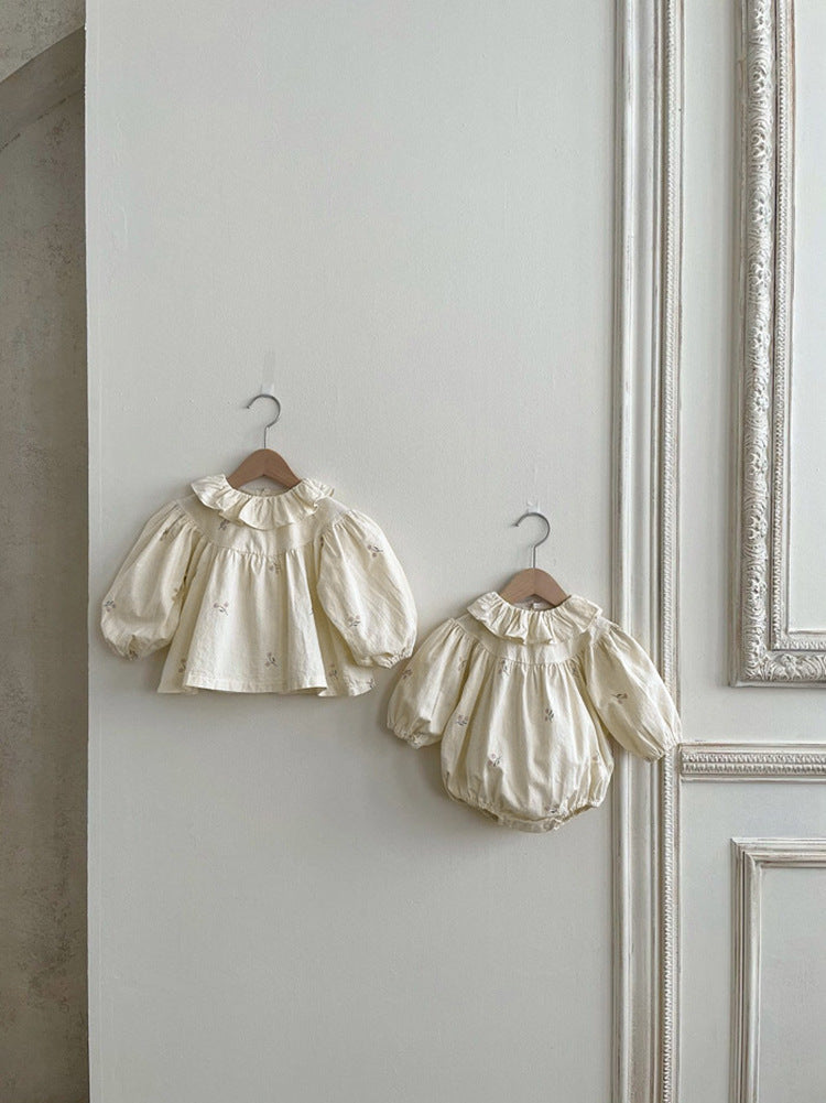 Baby girl wearing a flower embroidered onesie with ruffle lapel design in beige color, showcasing comfort and style.