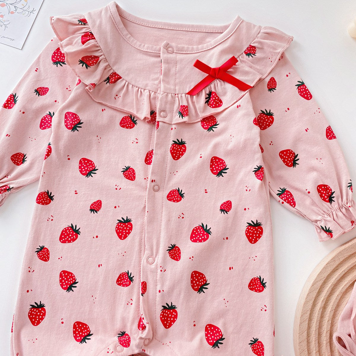 Baby girl romper featuring an allover strawberries pattern with ruffle design and button front, available in white and pink colors.
