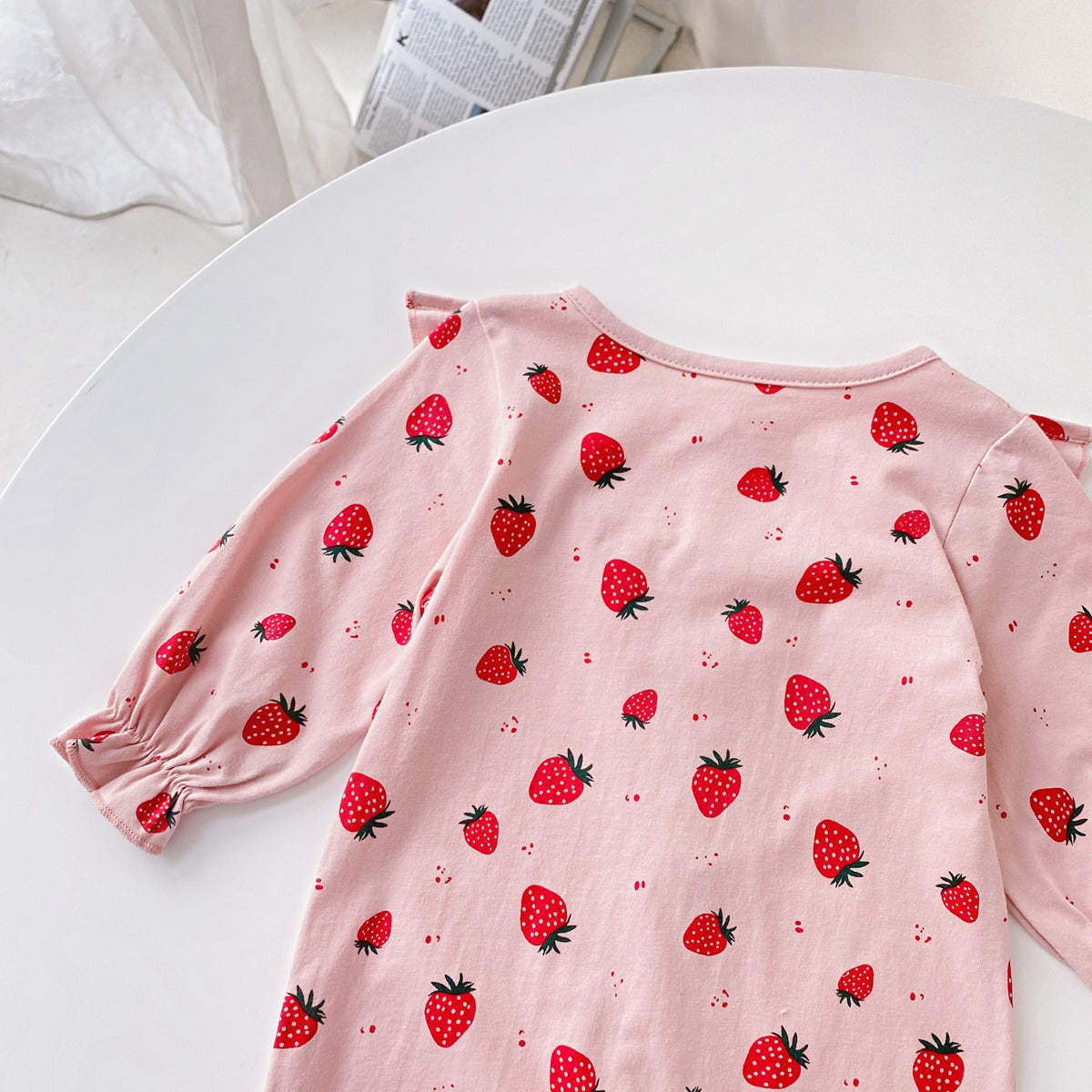 Baby girl romper featuring an allover strawberries pattern with ruffle design and button front, available in white and pink colors.