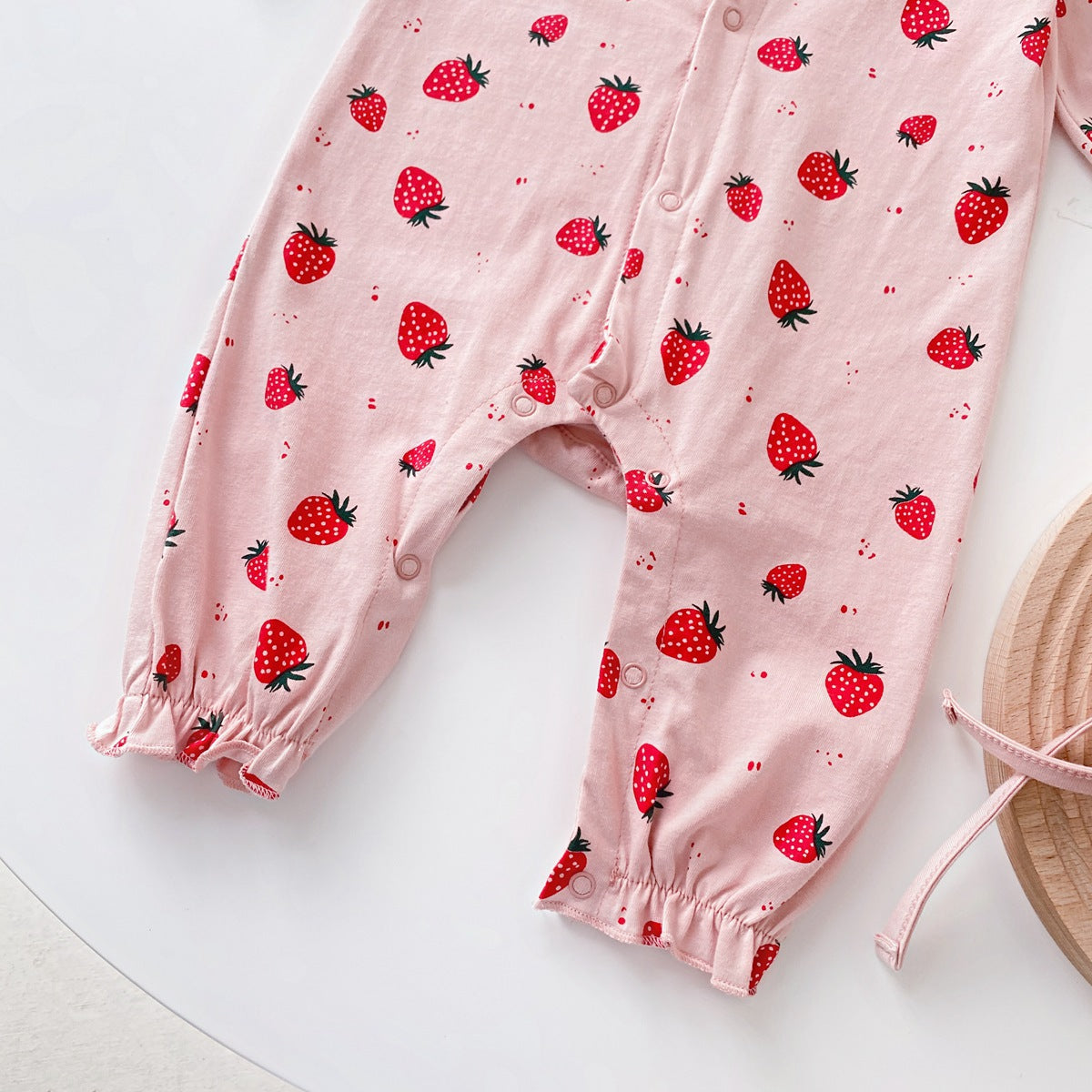 Baby girl romper featuring an allover strawberries pattern with ruffle design and button front, available in white and pink colors.