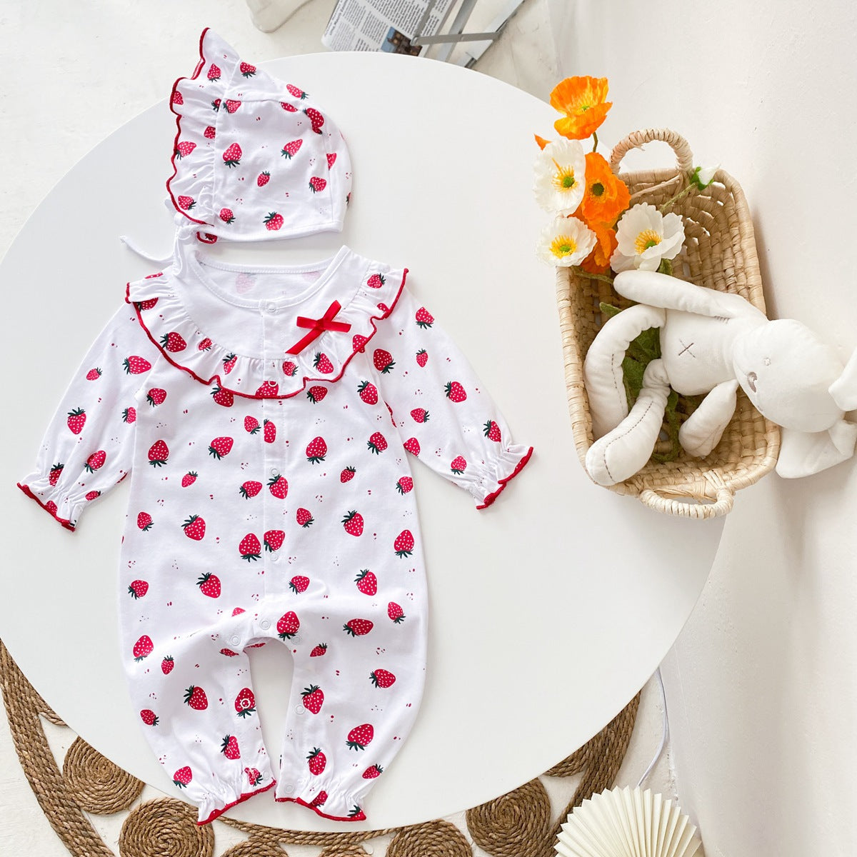 Baby girl romper featuring an allover strawberries pattern with ruffle design and button front, available in white and pink colors.