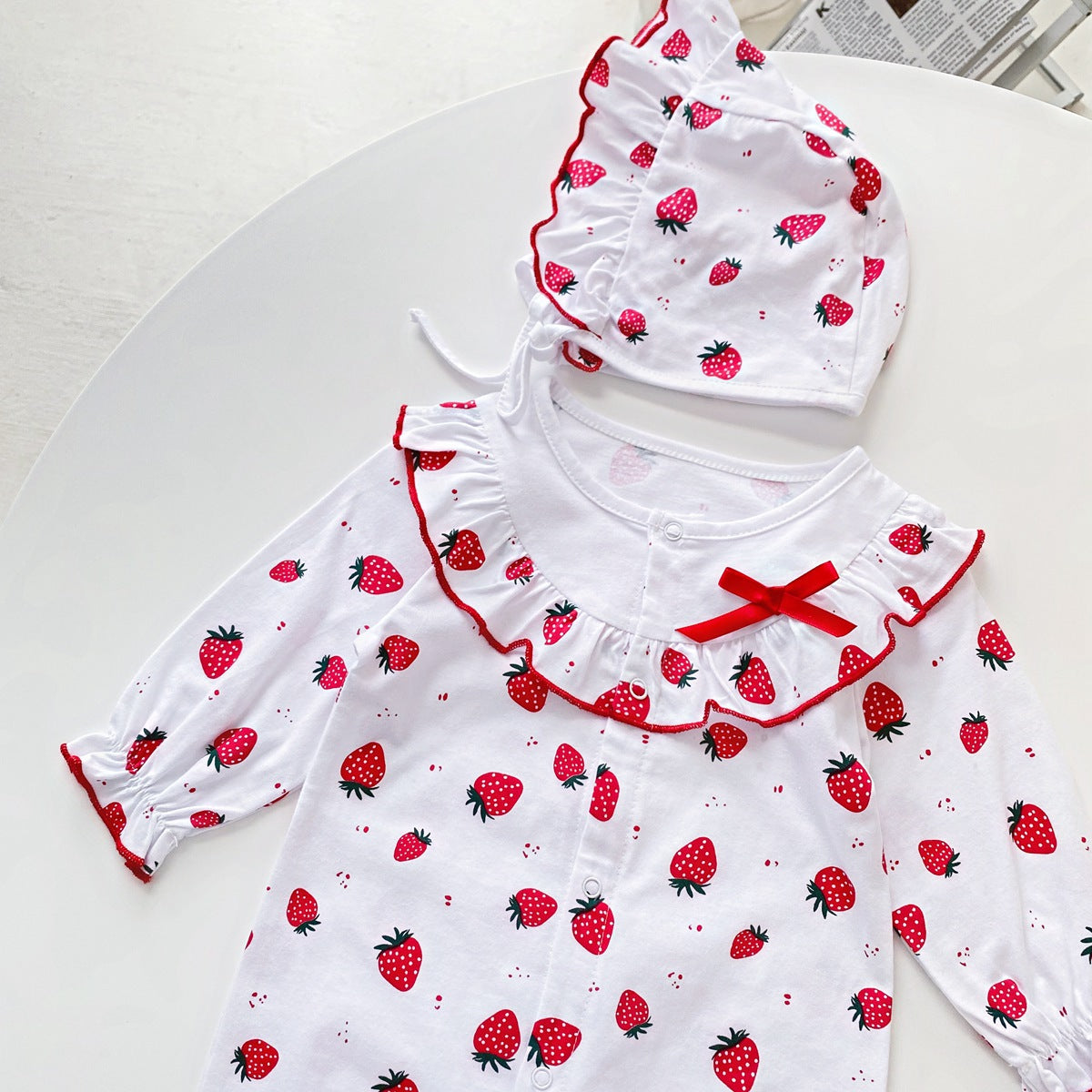 Baby girl romper featuring an allover strawberries pattern with ruffle design and button front, available in white and pink colors.