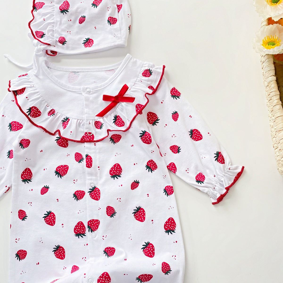 Baby girl romper featuring an allover strawberries pattern with ruffle design and button front, available in white and pink colors.