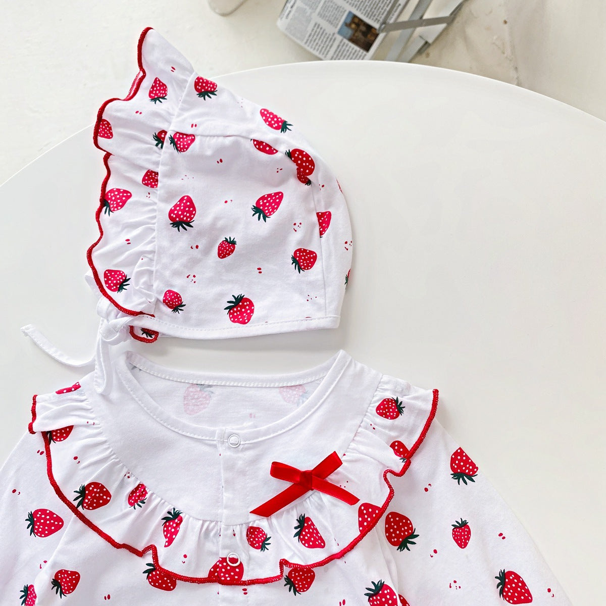 Baby girl romper featuring an allover strawberries pattern with ruffle design and button front, available in white and pink colors.