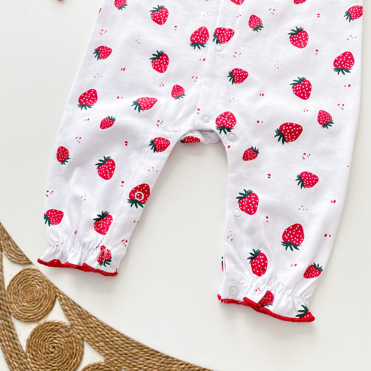 Baby girl romper featuring an allover strawberries pattern with ruffle design and button front, available in white and pink colors.