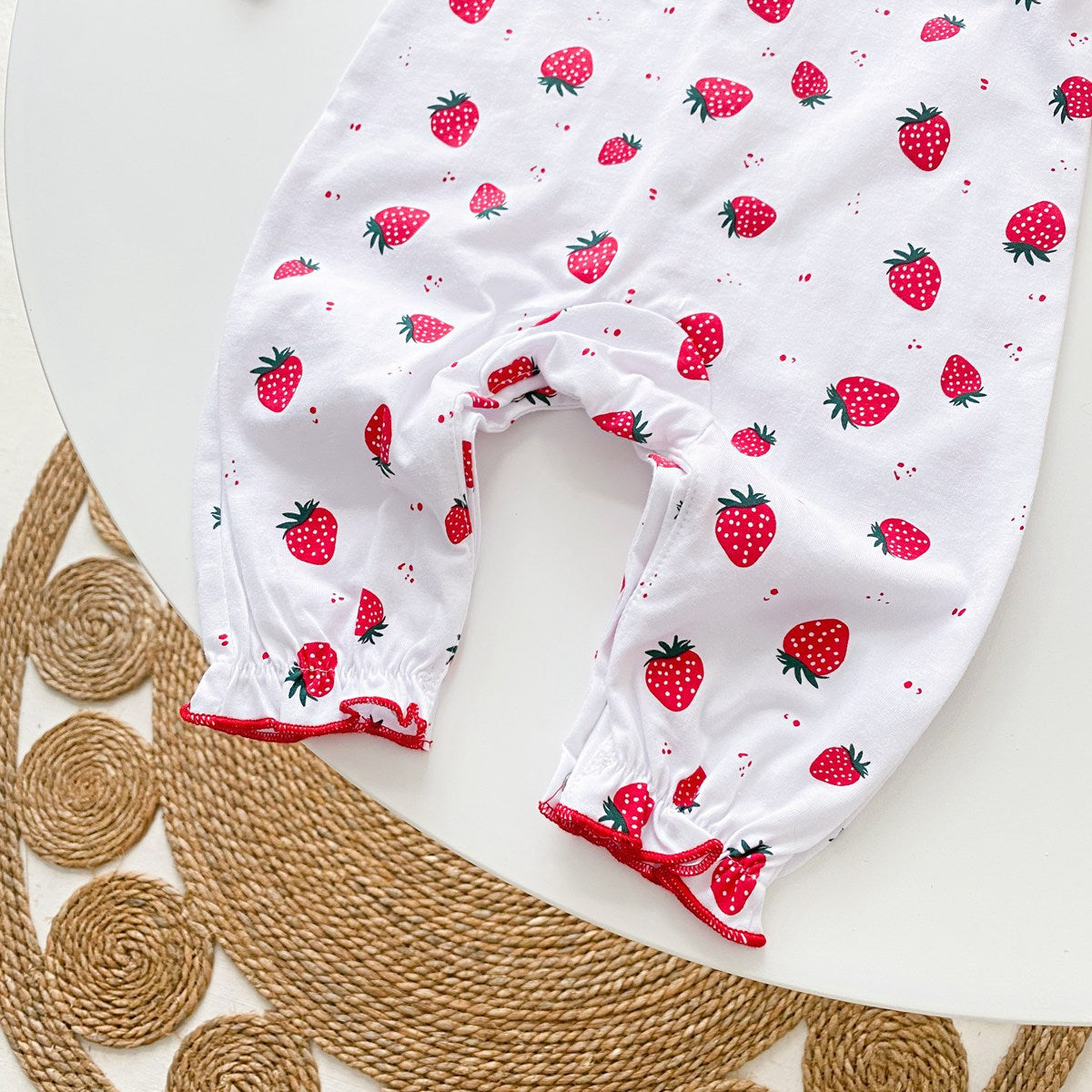 Baby girl romper featuring an allover strawberries pattern with ruffle design and button front, available in white and pink colors.