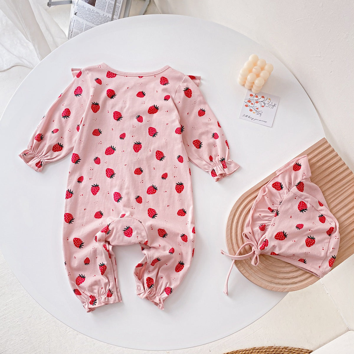 Baby girl romper featuring an allover strawberries pattern with ruffle design and button front, available in white and pink colors.