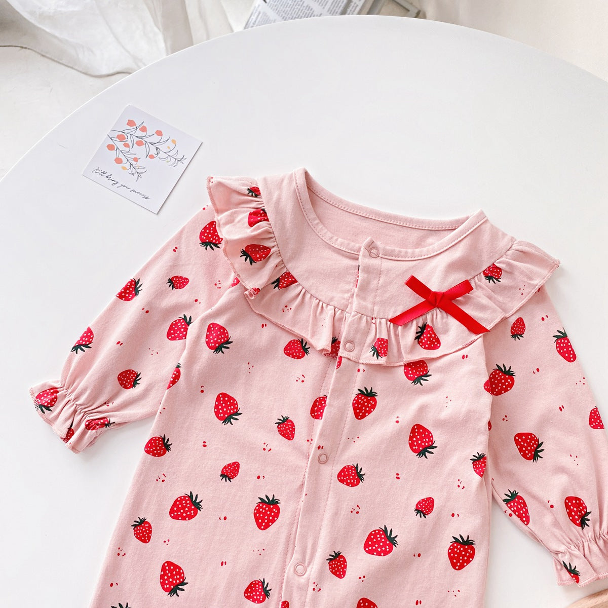 Baby girl romper featuring an allover strawberries pattern with ruffle design and button front, available in white and pink colors.