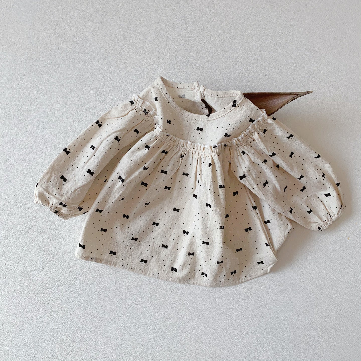 Baby girl wearing a stylish bow and polka dot A-line long sleeves shirt combo in apricot color.