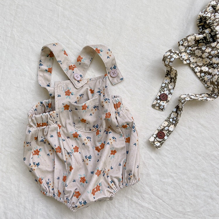 Baby girl wearing a cute floral print overall triangle onesie with straps in yellow color.