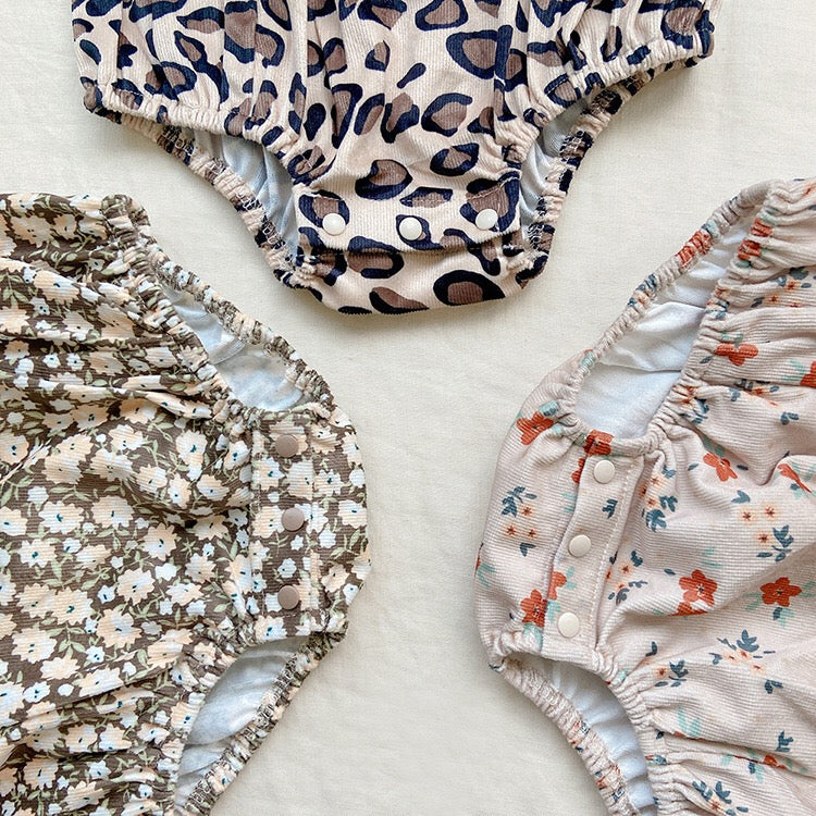 Baby girl wearing a cute floral print overall triangle onesie with straps in yellow color.