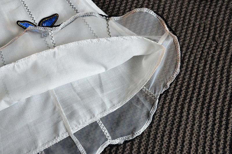 A charming white sleeveless dress for baby girls featuring dimensional butterfly embroidery and lace patchwork, perfect for summer occasions.