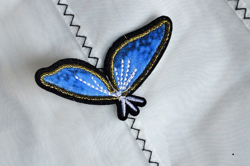 A charming white sleeveless dress for baby girls featuring dimensional butterfly embroidery and lace patchwork, perfect for summer occasions.