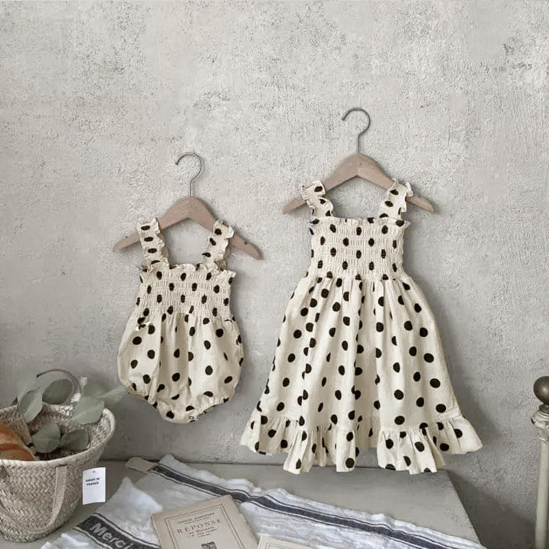 Baby girl wearing a beige and apricot polka dot sling onesie and dress, perfect for summer outings.