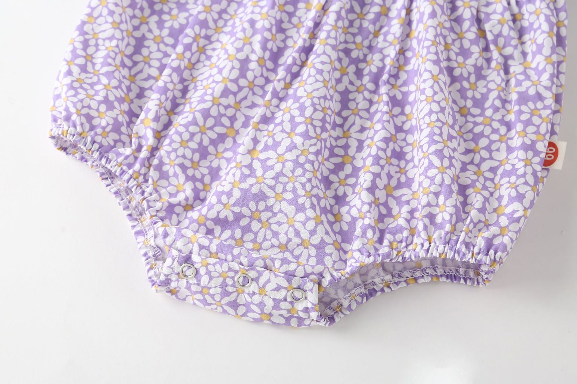 A vibrant baby girl onesie featuring a floral pattern and lace patchwork, with a round collar, in purple and orange colors.