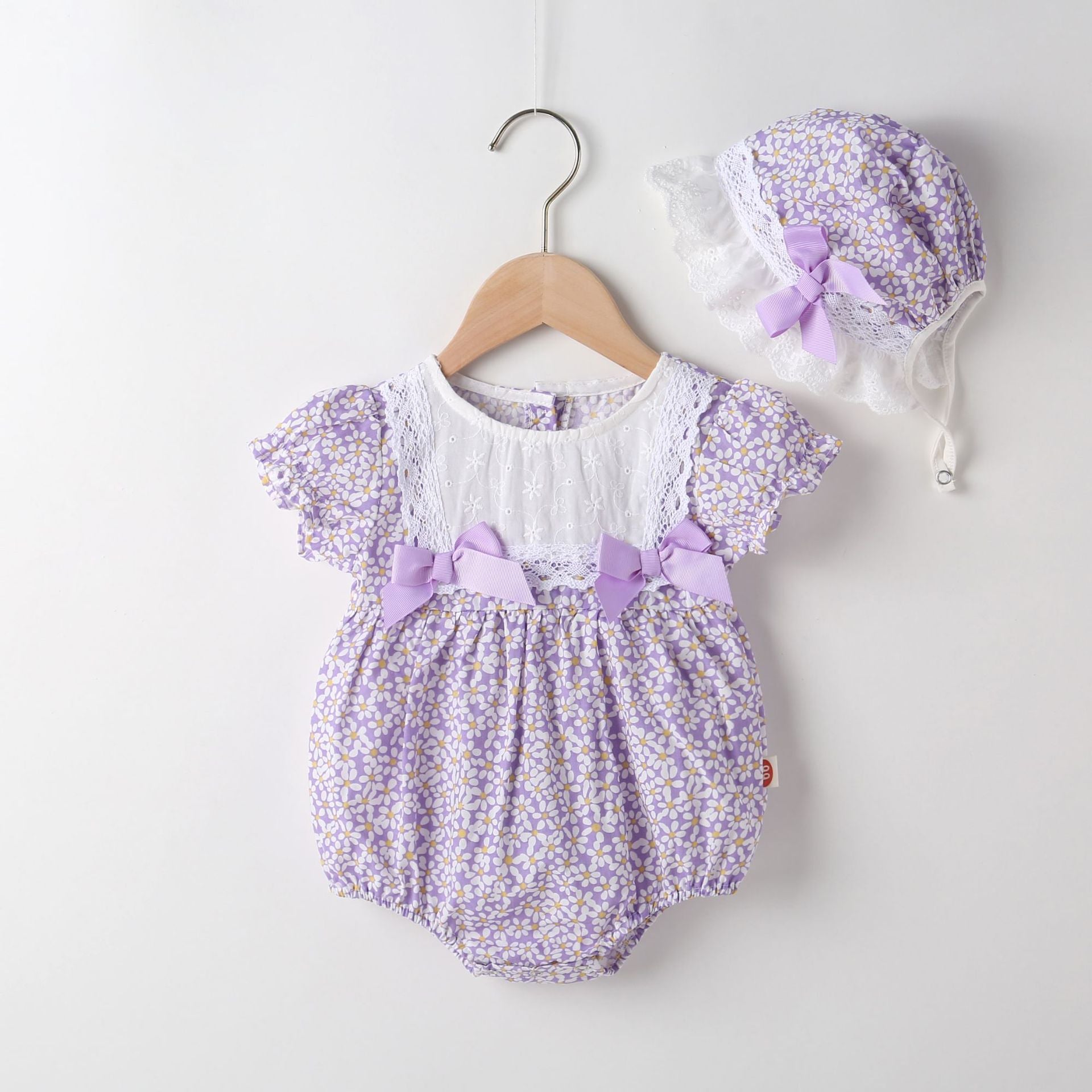A vibrant baby girl onesie featuring a floral pattern and lace patchwork, with a round collar, in purple and orange colors.