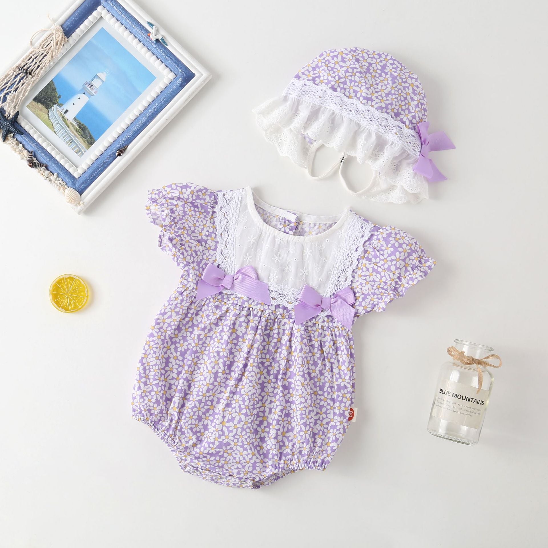 A vibrant baby girl onesie featuring a floral pattern and lace patchwork, with a round collar, in purple and orange colors.