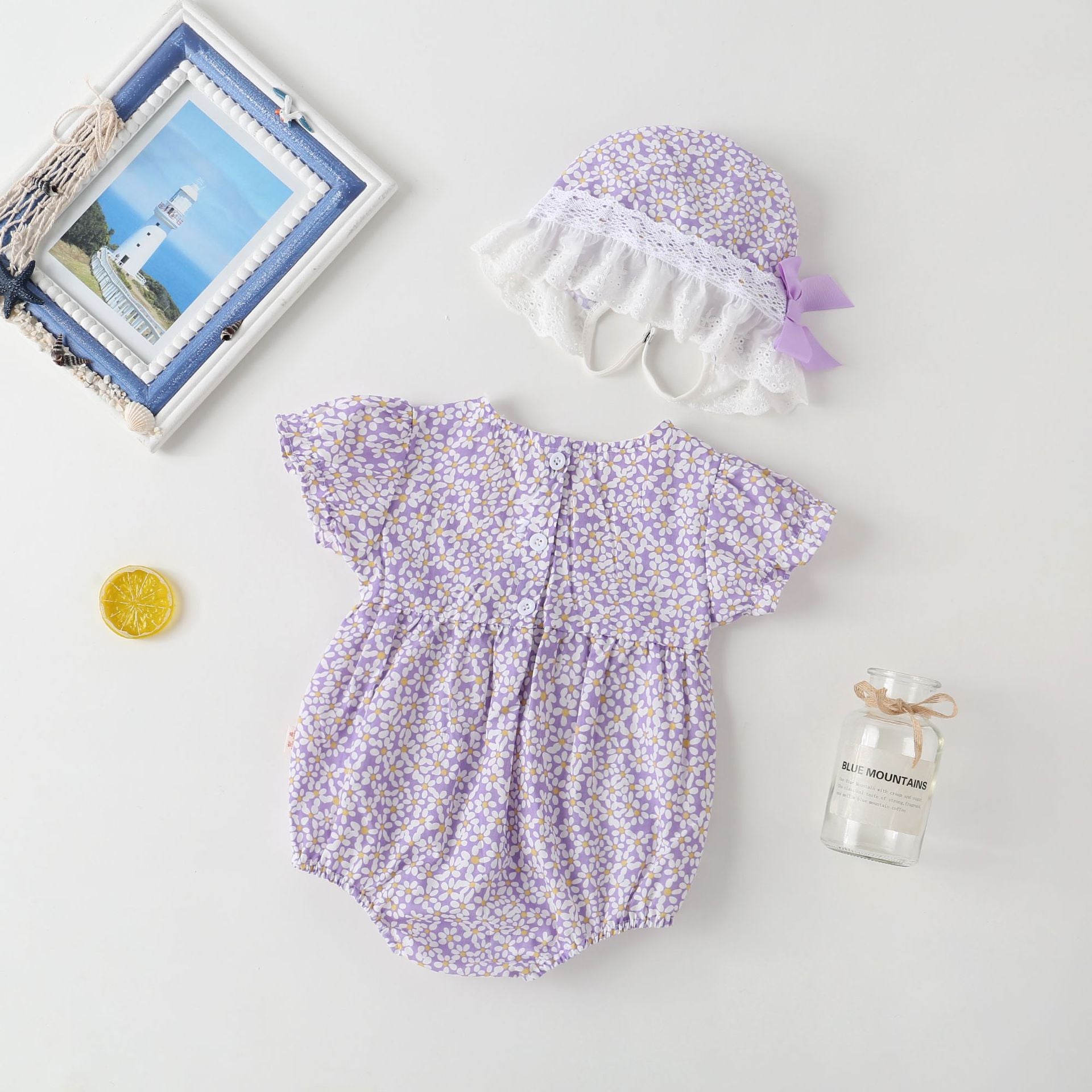 A vibrant baby girl onesie featuring a floral pattern and lace patchwork, with a round collar, in purple and orange colors.