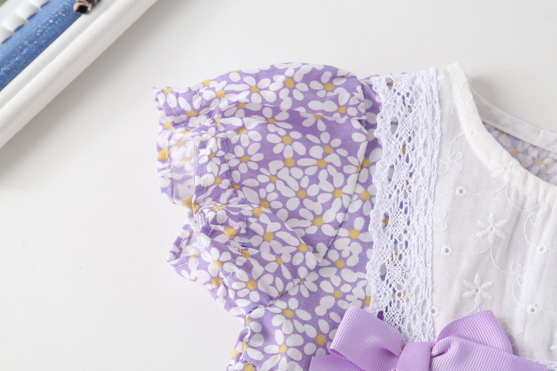 A vibrant baby girl onesie featuring a floral pattern and lace patchwork, with a round collar, in purple and orange colors.
