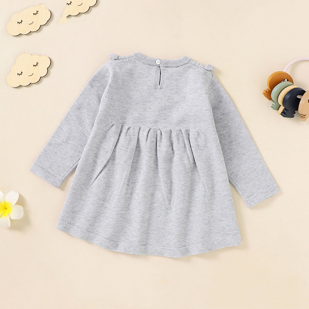 A baby girl wearing a soft knitted dress with flower patches in various colors, showcasing comfort and style.