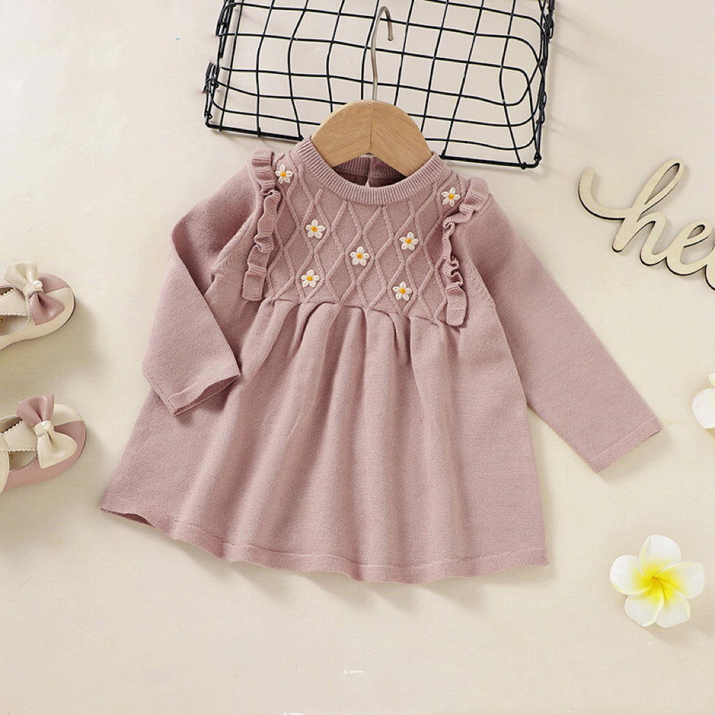 A baby girl wearing a soft knitted dress with flower patches in various colors, showcasing comfort and style.