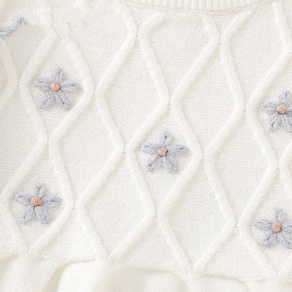 A baby girl wearing a soft knitted dress with flower patches in various colors, showcasing comfort and style.