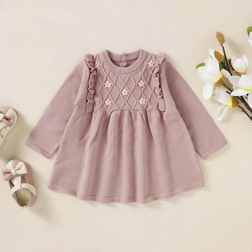 A baby girl wearing a soft knitted dress with flower patches in various colors, showcasing comfort and style.
