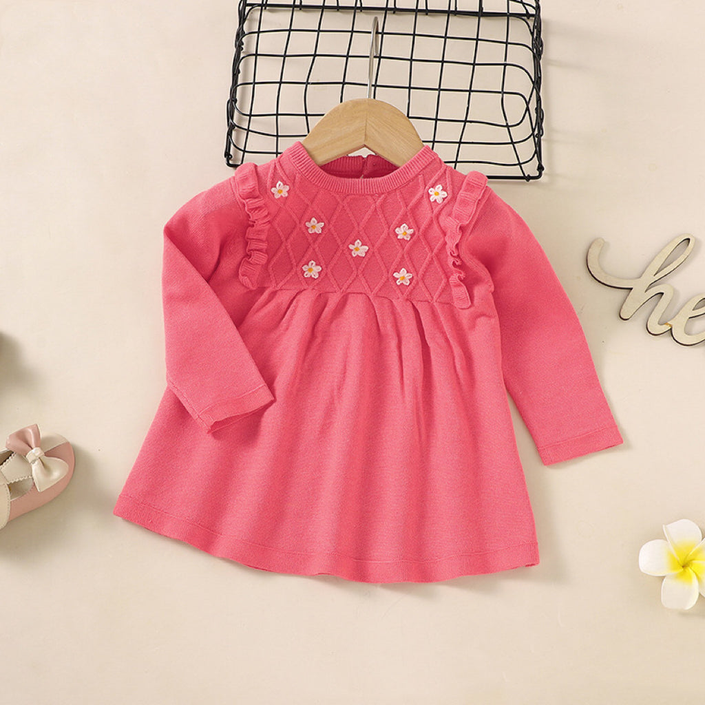 A baby girl wearing a soft knitted dress with flower patches in various colors, showcasing comfort and style.