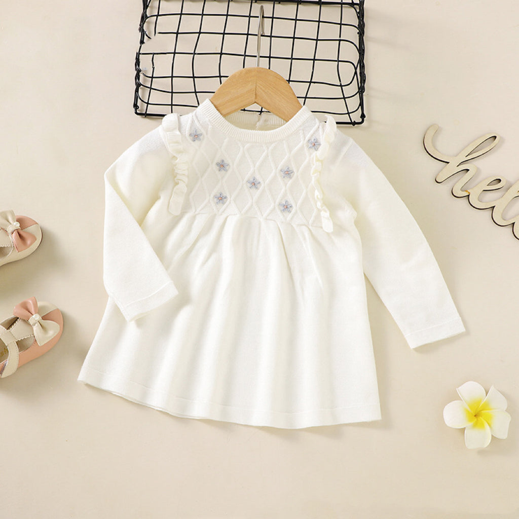 A baby girl wearing a soft knitted dress with flower patches in various colors, showcasing comfort and style.