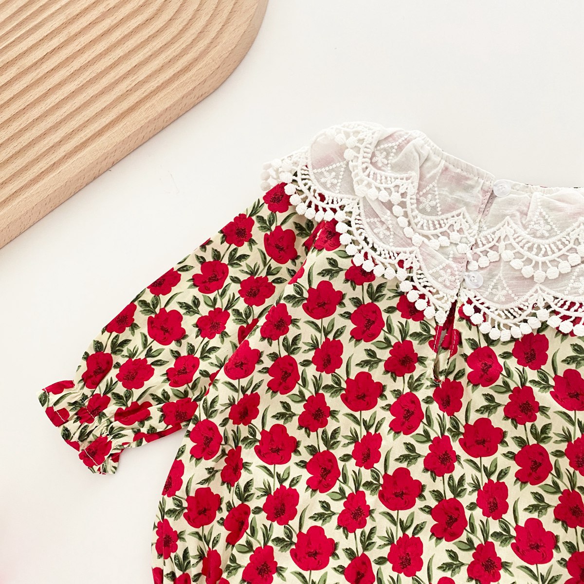 A baby girl wearing a flower-patterned bodysuit with a labeled collar and long sleeves in vibrant red and yellow colors.