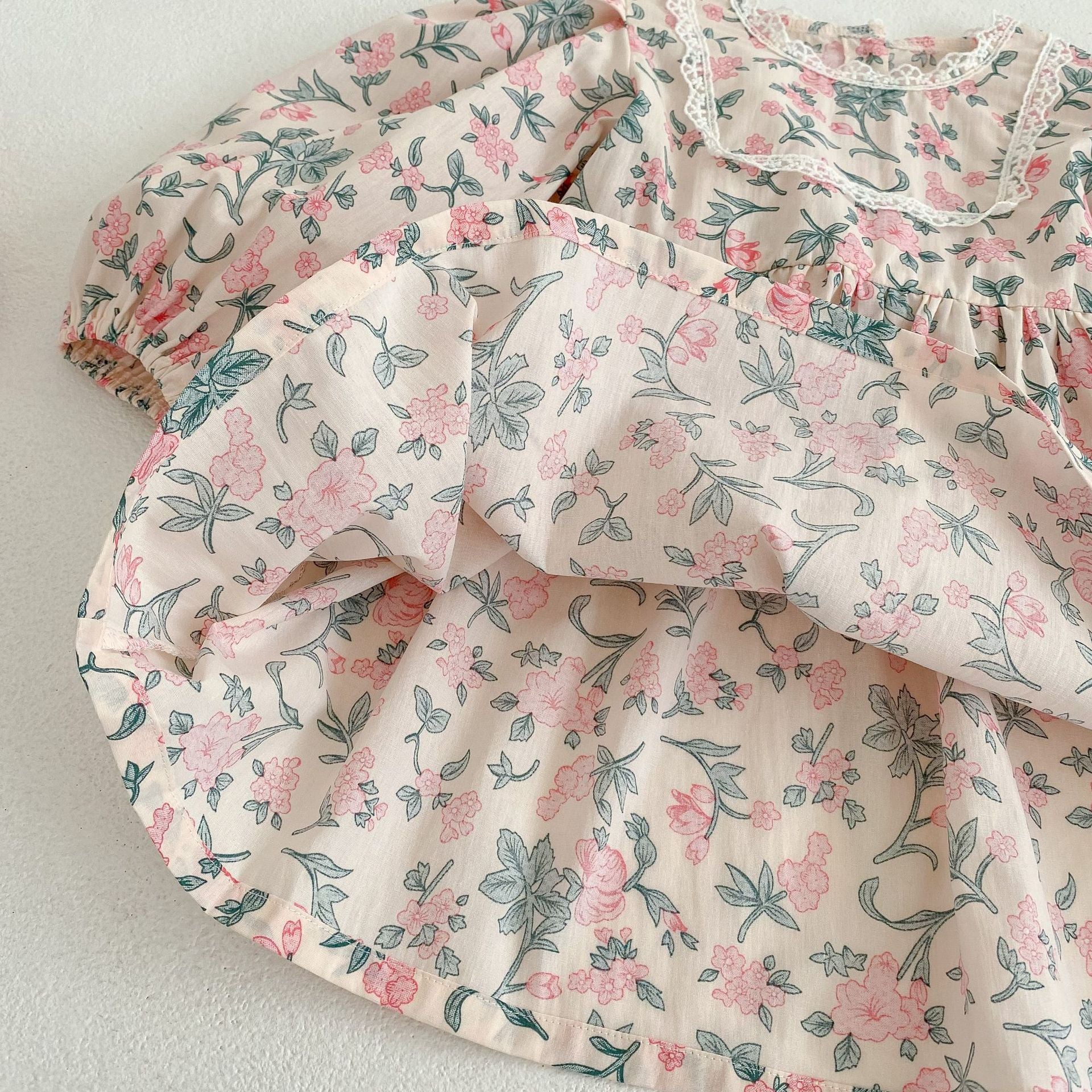 A cute baby girl wearing a floral print onesie and dress with mesh patchwork design in pink and light pink colors.