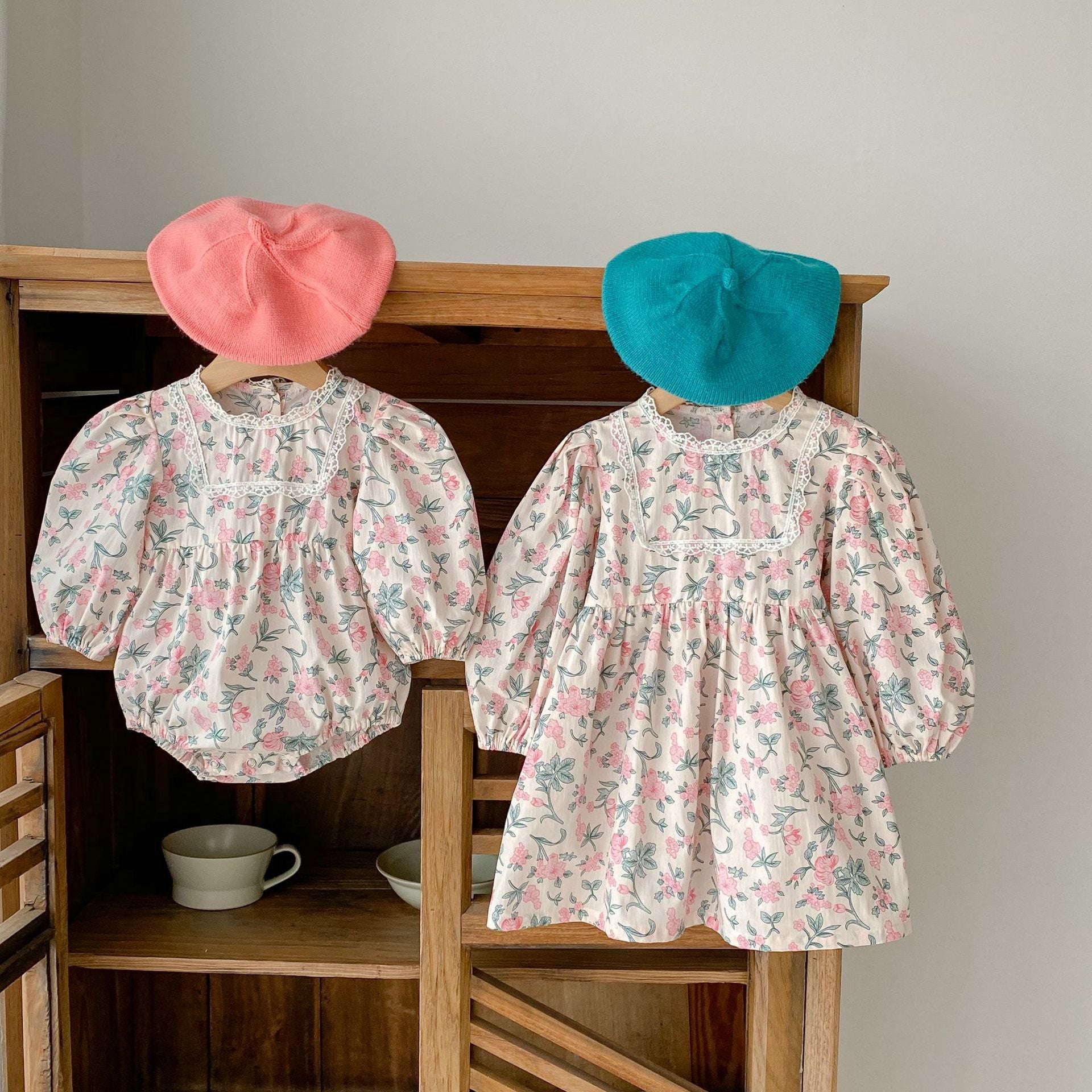 A cute baby girl wearing a floral print onesie and dress with mesh patchwork design in pink and light pink colors.